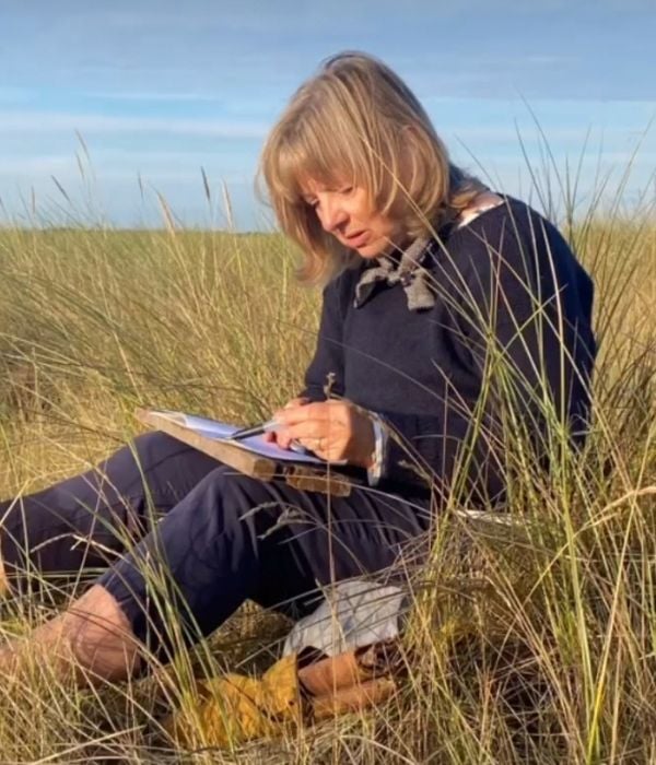 Artist Debbie Lyddon sitting in the grass sketching and taking notes