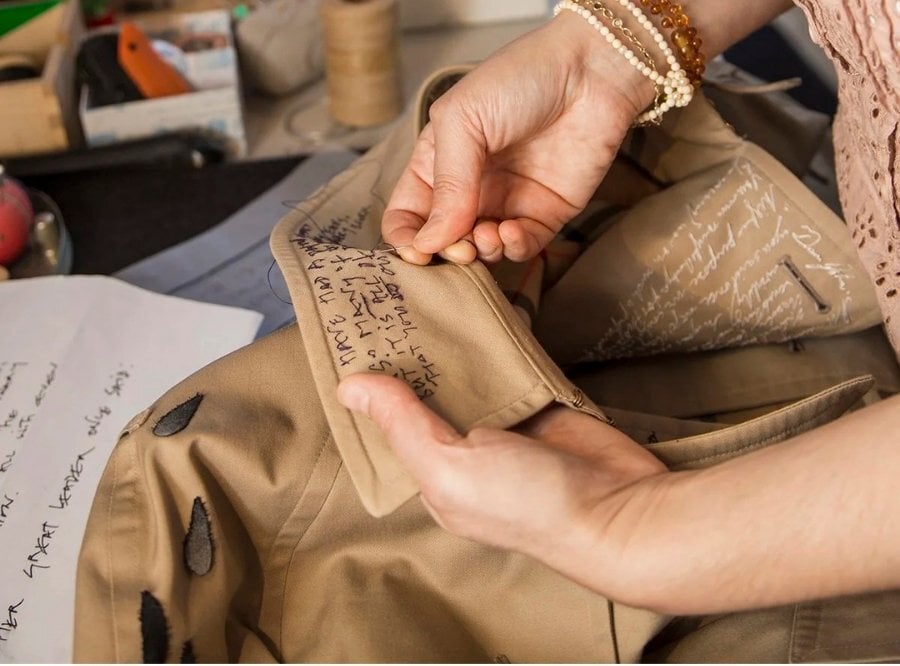 Close-up of Rosalind's hands as she hand-embroiders letters onto the collar of a shirt.