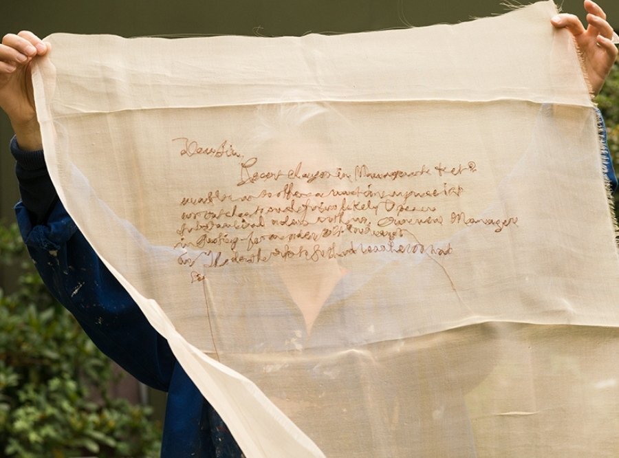 Rosalind Wyatt holding up a piece of cloth that she has hand-embroidered with letters.